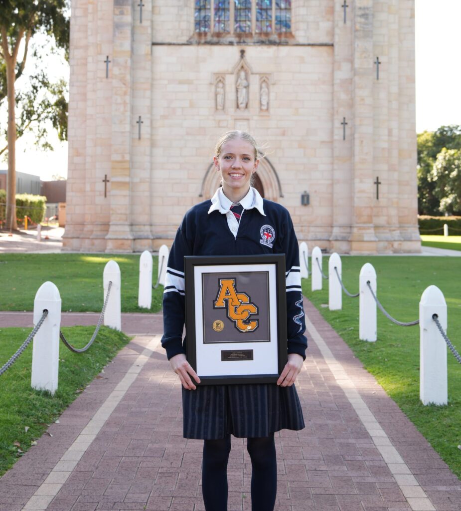 Guildford Grammar School student holding sports award outside church.