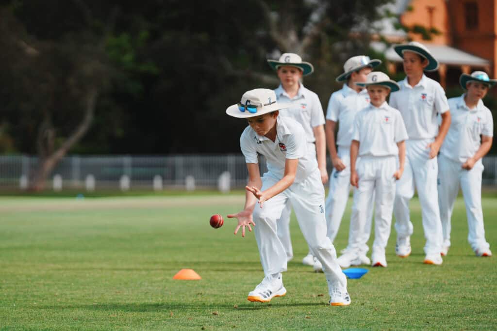 Guildford Grammar School students in white cricket whites fielding a ball.