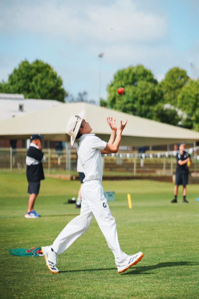 Cricketer in white uniform bowling during a match at Guildford Grammar School.