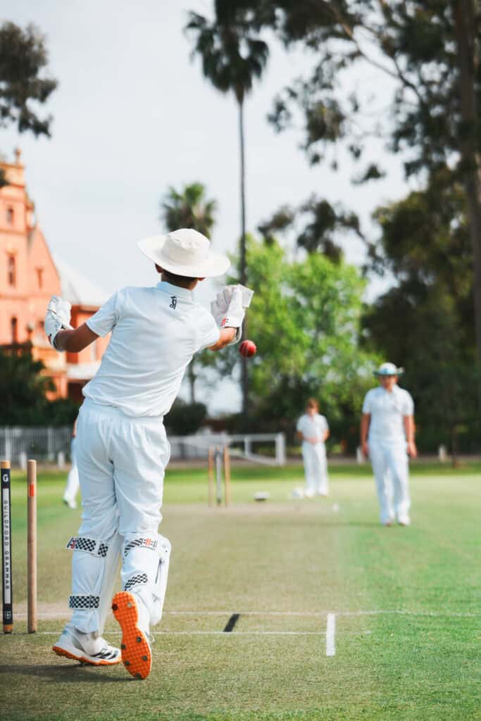 Cricketer in white cricket whites bowling on the field at Guildford Grammar School.
