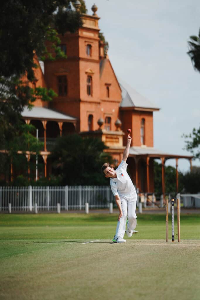 Cricketer delivering a fast ball on a sunny day at Guildford Grammar School cricket field.