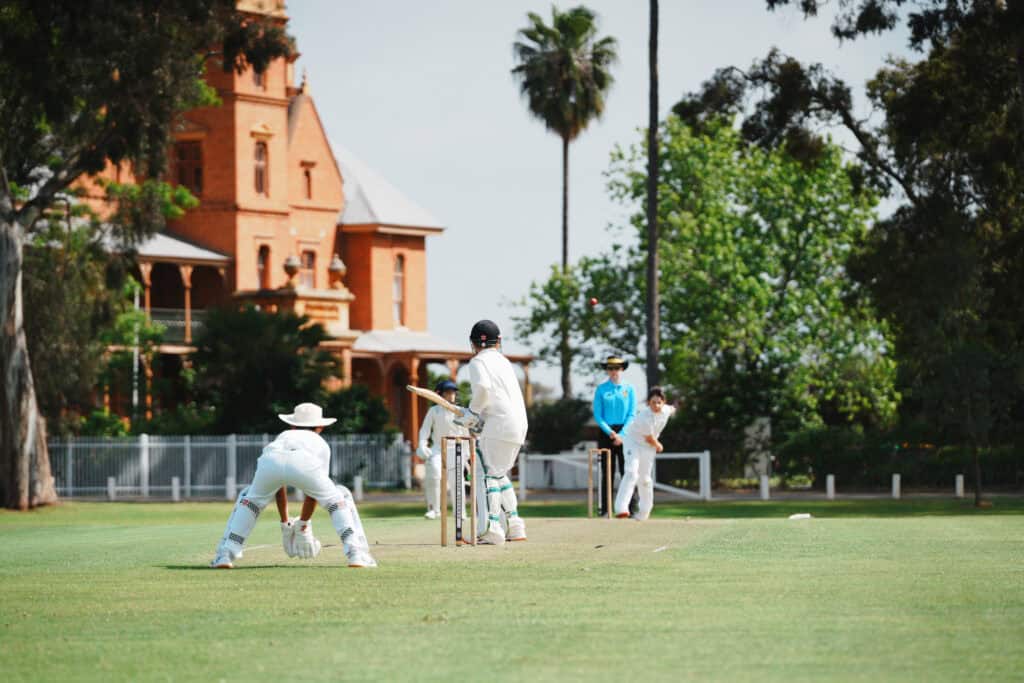 Cricket match at Guildford Grammar School grounds with players in white uniforms.